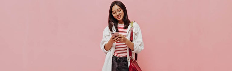 Young woman using smartphone against pink background