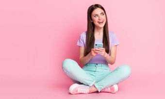 Woman sitting on floor looking at phone against light pink background