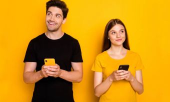 Young couple using phones against yellow background