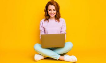 Woman happily using laptop while sitting cross-legged
