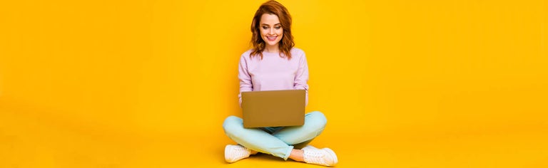Woman happily using laptop while sitting cross-legged