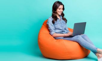 Woman looking at laptop sitting on bean bag against teal background