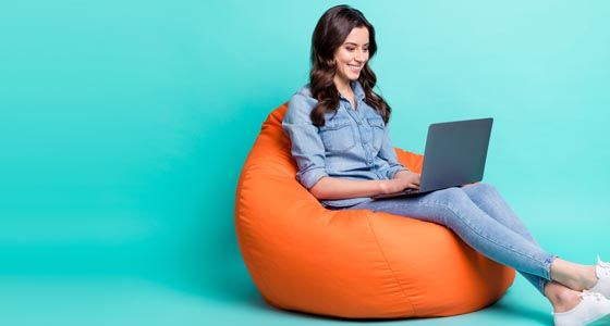 Woman looking at laptop sitting on bean bag against teal background