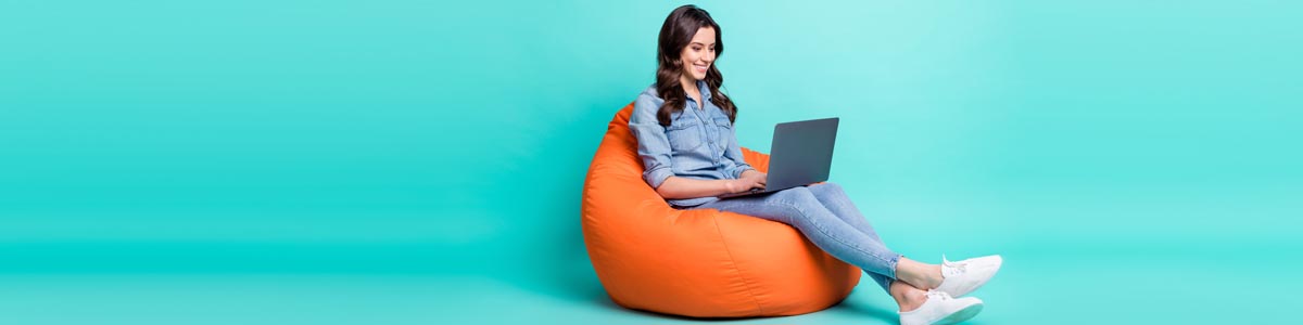 Woman looking at laptop sitting on bean bag against teal background