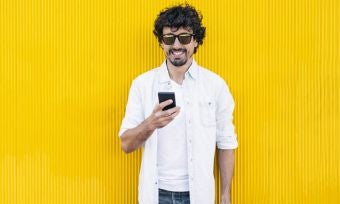 Young man using phone against yellow wall