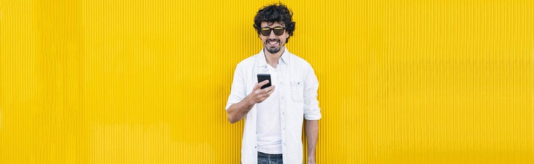 Young man using phone against yellow wall