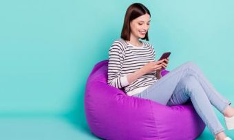 Woman looking at phone sitting on purple beanbag against teal background