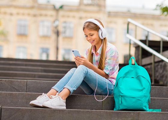 Girl looking at phone, wearing headphones and sitting on stairs with backpack