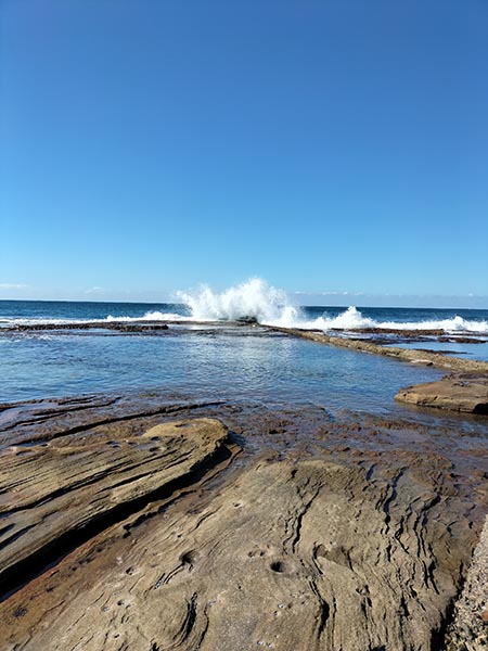 Photo of waves crashing on rock pool on clear day