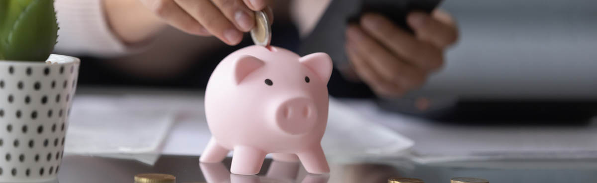 Woman with smartphone putting coin in piggy bank