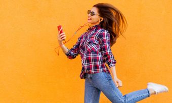 Young woman using smartphone against orange wall