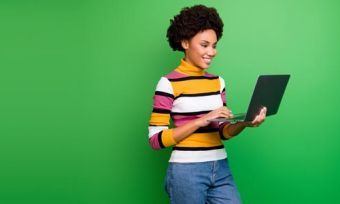 Young woman holding and looking at laptop against green background