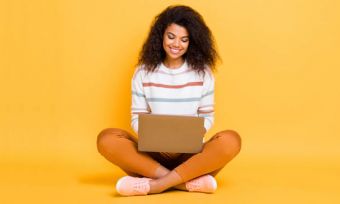 Happy woman using laptop against yellow background