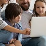 A family sitting on a couch using a laptop