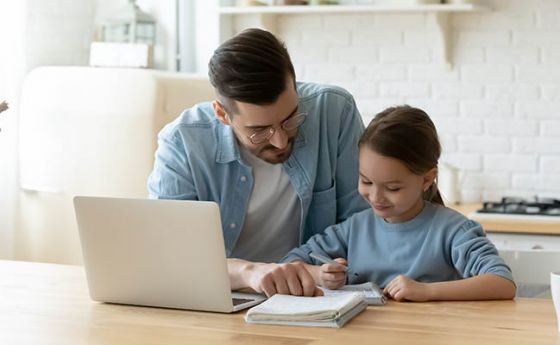 Father helping daughter with homework at laptop