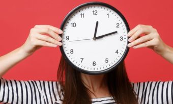 Woman holding clock over face signifying long wait times with red background