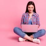 Young woman looking at laptop against pink background