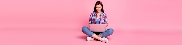 Young woman looking at laptop against pink background