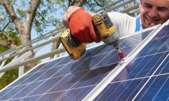 Solar installer drilling in PV panels on rooftop