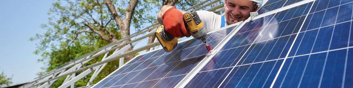 Solar installer drilling in PV panels on rooftop