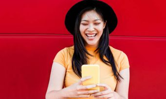 Smiling young woman in yellow using phone against red wall