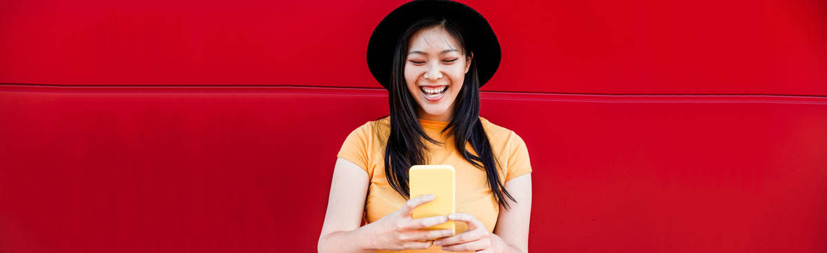 Smiling young woman in yellow using phone against red wall