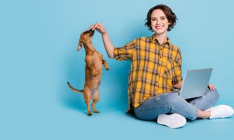 Woman with laptop and playing with dog against blue background
