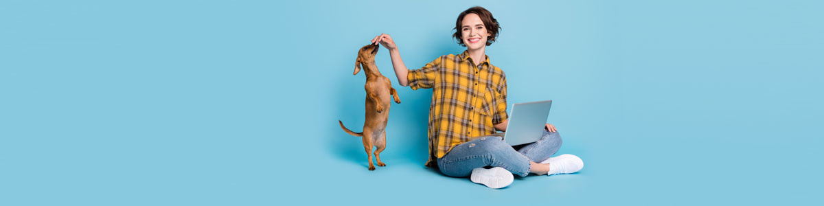 Woman with laptop and playing with dog against blue background