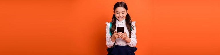 Girl in school uniform with backpack looking at phone against orange background