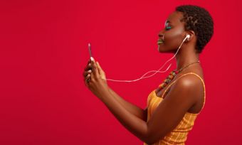 Woman looking at phone with headphones on against red background