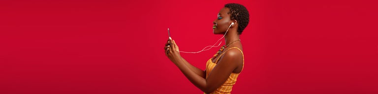 Woman looking at phone with headphones on against red background