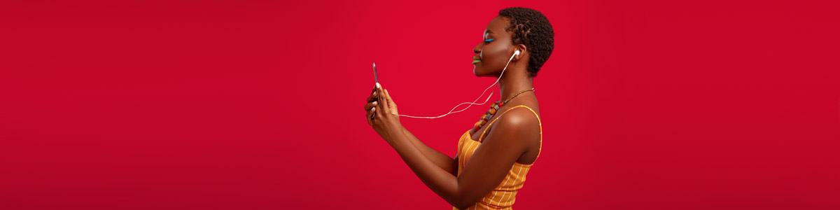 Woman looking at phone with headphones on against red background