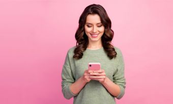 Woman looking at mobile phone against pink background