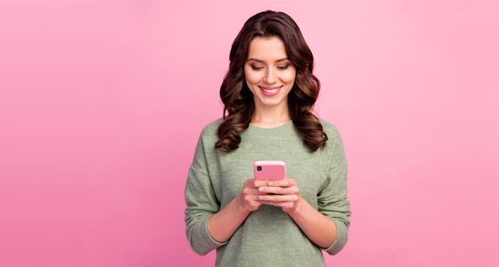 Woman looking at mobile phone against pink background