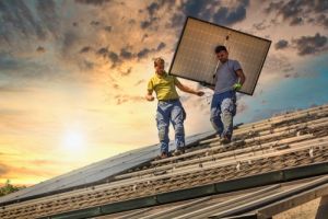 Two men carrying solar panel on roof