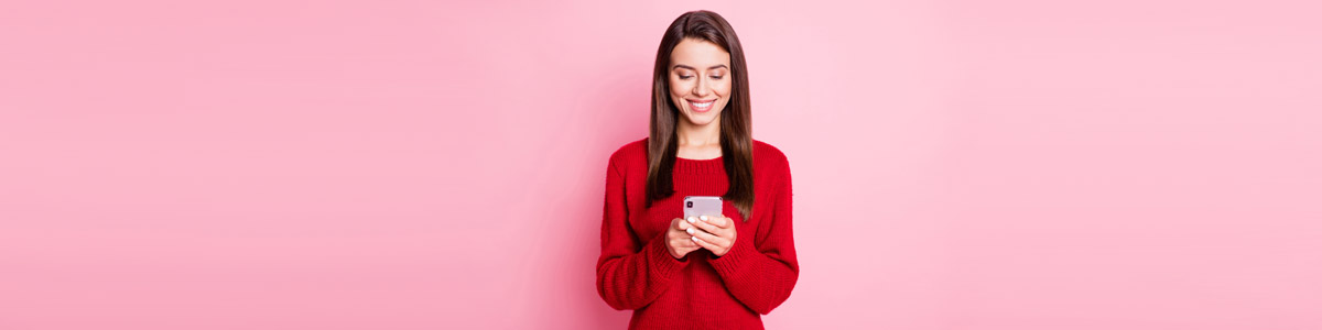 Woman looking at phone against pink background