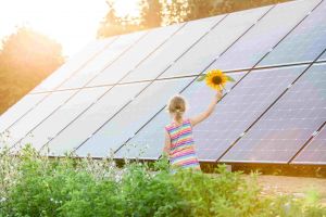 Little girl walking past solar panels with a sunflower in her hand 