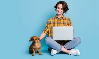 Smiling young woman using laptop with small brown dog