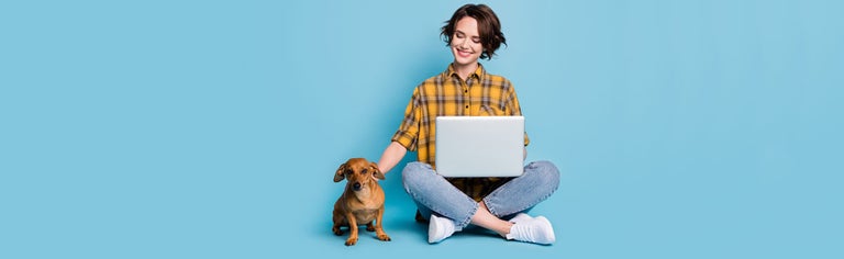 Smiling young woman using laptop with small brown dog