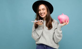 Happy young woman holding smartphone and piggy bank