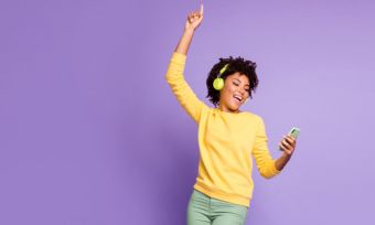 Woman listening to music and holding phone against purple background