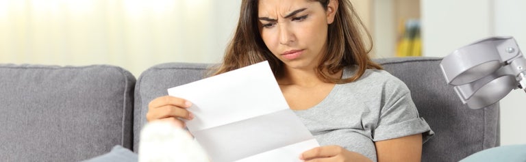 Lady sitting on couch with energy bill looking confused