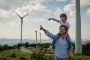 Dad with daughter on shoulders looking at wind turbines, smiling. 