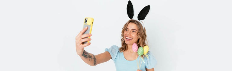 Young woman taking selfie with rabbit ears and Easter eggs