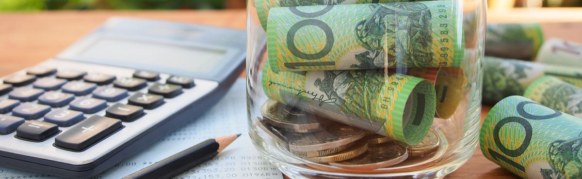 Jar with $100 notes in it next to notebook and calculator