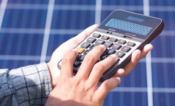 Man holding calculator in front of solar panels