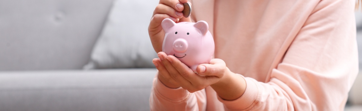 Person putting coins in a pink piggy bank