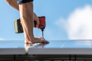 Hand with drill installing solar panels on roof