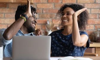 Man and woman high-fiving with laptop in front of them