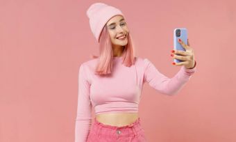 Young pink-haired woman using phone against pink background